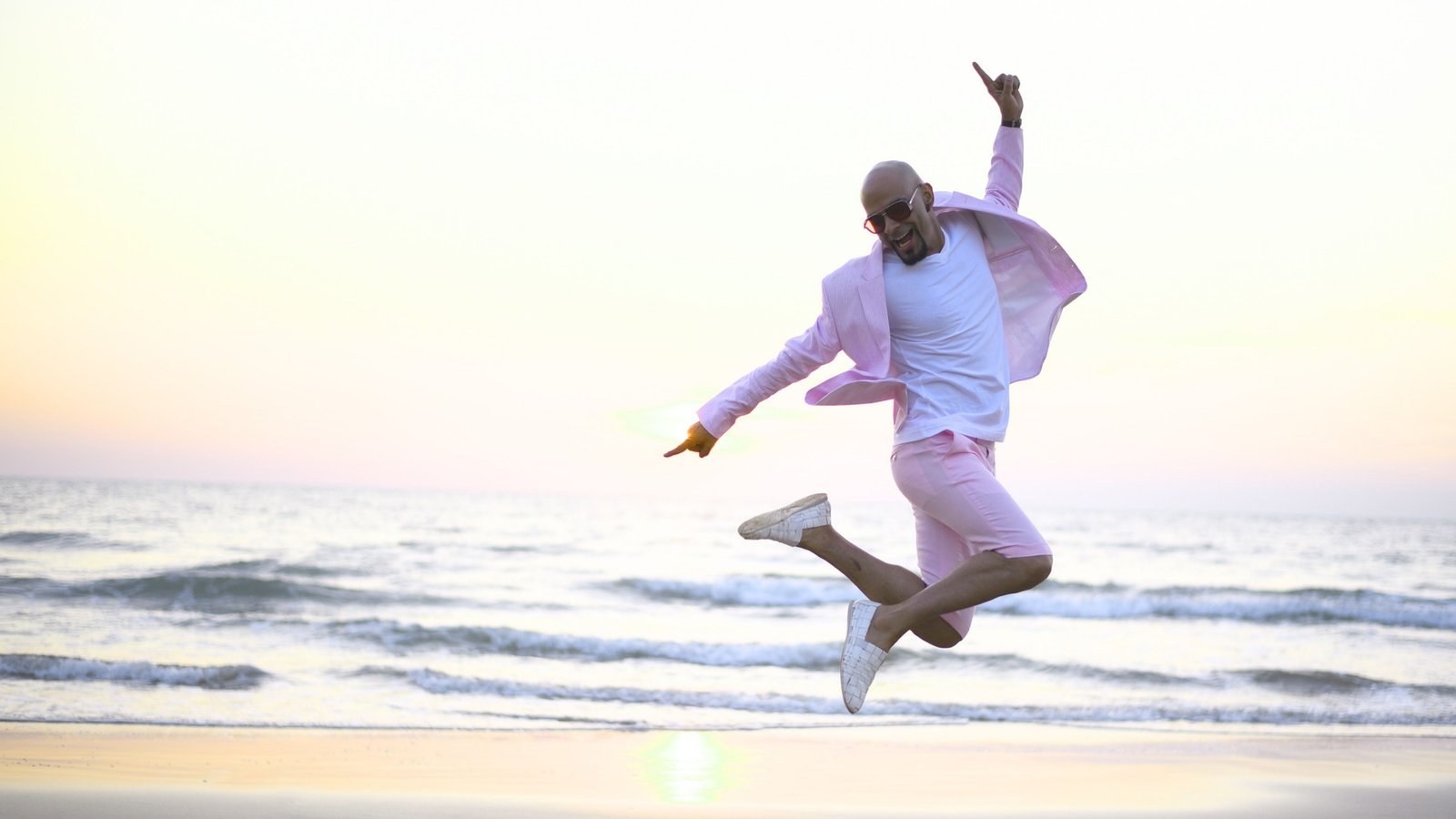 Groom jumping joyfully on the beach at sunset